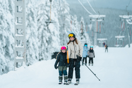 Vuxen och barn med skidor vid lift i snötäckt backe